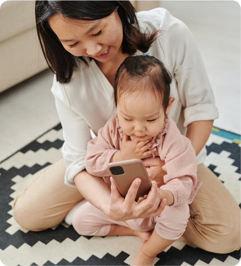 A mother is holding her baby in her arms while both look at a smartphone screen together.